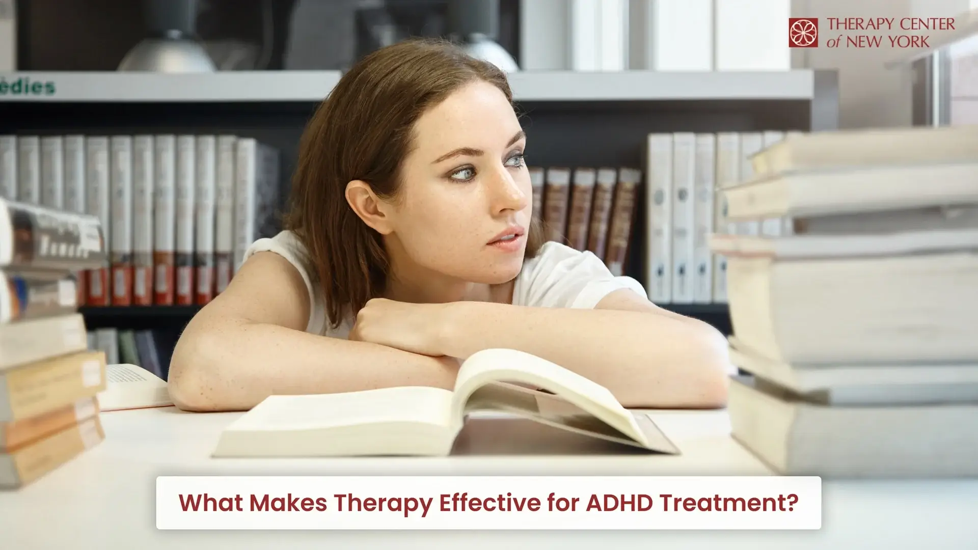 Young woman struggling to focus while studying with books around her, representing challenges related to ADHD treatment and therapy.